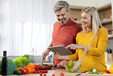 Man and woman referring to a tablet while cooking in the kitchen